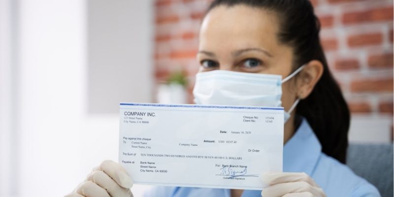 Female business owner in mask holding up PPP funding cheque during Coronavirus pandemic